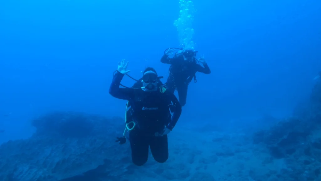 Two scuba divers waving underwater at Caño Island